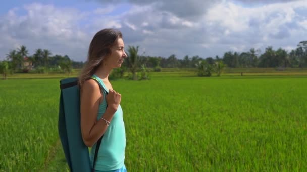 Slowmotion steadicam tiro de uma jovem mulher com ioga matemática andando através de um belo campo de arroz — Vídeo de Stock