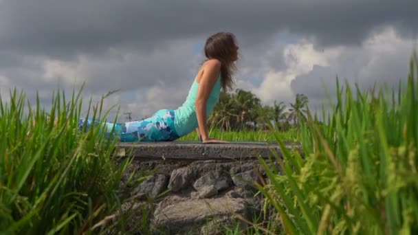 Slowmotion Steadicam skott av en ung kvinna som tränar yoga på ett vackert risfält — Stockvideo