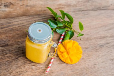 Eski ahşap arka planda çizgili kırmızı pipetli cam mason kavanozundaki mangodan sulu smoothie. Sağlıklı yaşam konsepti, kopyalama alanı