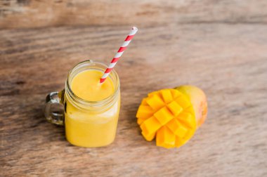 Eski ahşap arka planda çizgili kırmızı pipetli cam mason kavanozundaki mangodan sulu smoothie. Sağlıklı yaşam konsepti, kopyalama alanı
