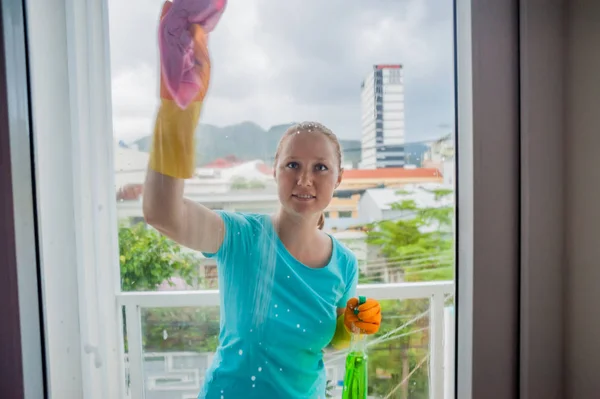 Hermosa doncella haciendo las tareas domésticas mientras usa un spray, lavando ventanas — Foto de Stock