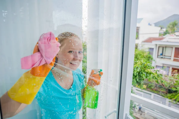 Hermosa doncella haciendo las tareas domésticas mientras usa un spray, lavando ventanas — Foto de Stock