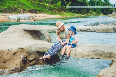 Anne ve küçük oğlu nehrin arka plan üzerinde köprü üzerinde oturan