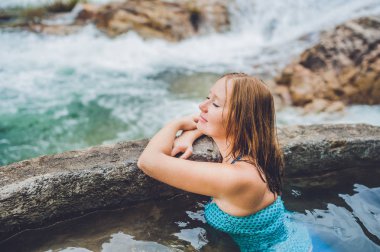 Jeotermal kaplıca. Bir şelalenin arka planına karşı kaplıca havuzunda dinlenen kadın