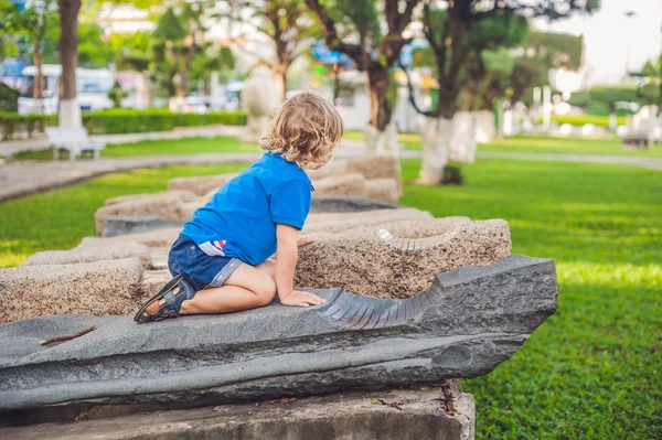 Rapaz louro bonito sobe os blocos de pedra no parque infantil. Infância, conceito — Fotografia de Stock