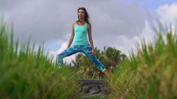 Plan au ralenti d'une jeune femme pratiquant le yoga sur un beau champ de riz — Video