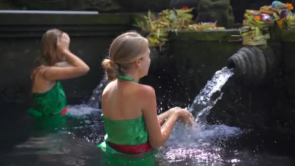 Filmagem em câmara lenta de duas jovens mulheres visitando as nascentes de azevinho na Indonésia. Tirta Empul nasce água benta na ilha de Bali — Vídeo de Stock