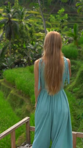 Vídeo vertical. Uma bela jovem em um vestido azul visita o famoso Tegalalalang Rice Terraces na aldeia de Ubud, na ilha de Bali — Vídeo de Stock