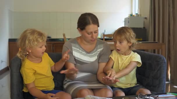 En lärare, en handledare för hemundervisning. en lärare eller mamma vid bordet med liten flicka och pojke. Hemskolekoncept — Stockvideo