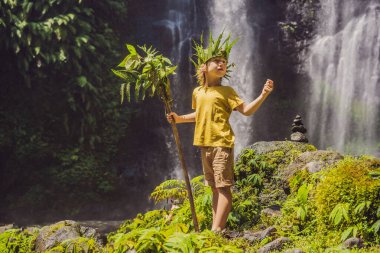 Tatlı çocuk ormanın kralını bir şelalenin arka planında tasvir ediyor. Aletsiz çocukluk kavramı. Çocuk konseptiyle seyahat etmek. Çocukluk kavramı.