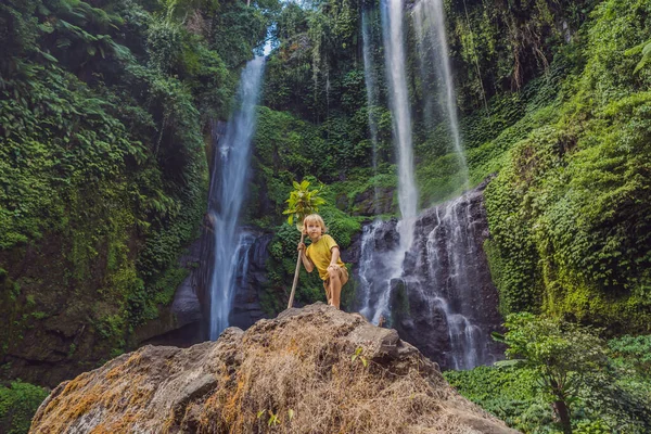 Rapaz bonito retrata o rei da selva contra o pano de fundo de uma cachoeira. Infância sem conceito de gadgets. Viajar com conceito de crianças. Conceito de infância ao ar livre — Fotografia de Stock