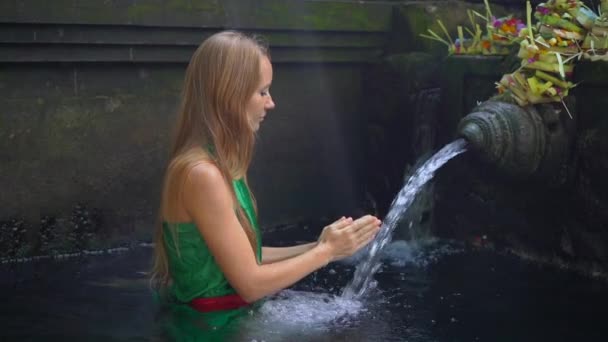 Filmagem em câmara lenta de uma jovem visitando as nascentes de azevinho na Indonésia. Tirta Empul nasce água benta na ilha de Bali — Vídeo de Stock