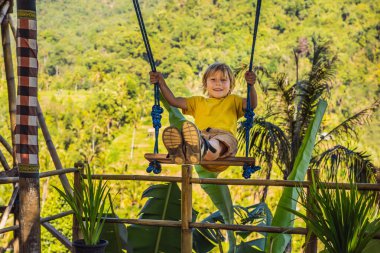 Endonezya'nın Bali adasının orman yağmur ormanlarında sallanan genç çocuk. Tropik lerde salıncak. Swings - Bali trendi. Çocuk konsepti ile seyahat. Çocuklarla ne yapmalı? Çocuk dostu bir yer