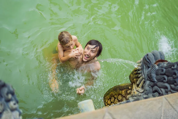 Papà e figlio viaggiatori in terme banjar. L'acqua termale viene rilasciata dalla bocca delle statue nelle sorgenti termali di Banjar, Bali, Indonesia. Viaggiare con i bambini concetto — Foto Stock