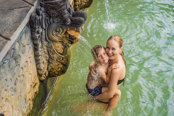 Viajeros de madre e hijo en aguas termales banjar. El agua termal se libera de la boca de estatuas en una fuente termal en Banjar, Bali, Indonesia. Viajar con concepto de niños — Foto de Stock