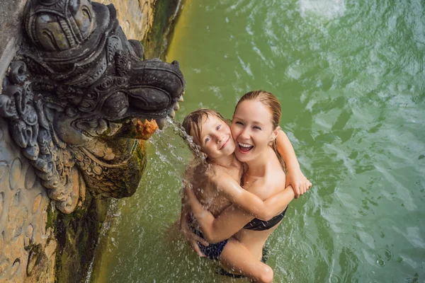 Mamma e figlio viaggiatori in terme banjar. L'acqua termale viene rilasciata dalla bocca delle statue nelle sorgenti termali di Banjar, Bali, Indonesia. Viaggiare con i bambini concetto — Foto Stock