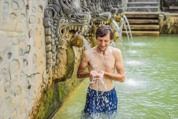 Un joven en un banjar de aguas termales. El agua termal se libera de la boca de estatuas en una fuente termal en Banjar, Bali, Indonesia — Foto de Stock