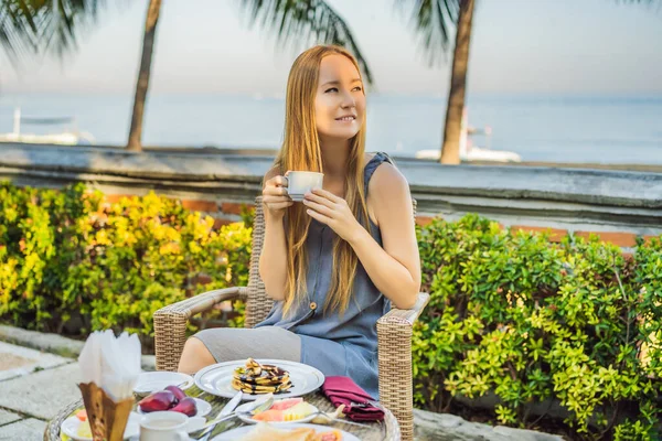 Young woman having romantic breakfast in sunrise at resort restaurant outdoor. Healthy food drink for breakfast. Beautiful woman at vacation