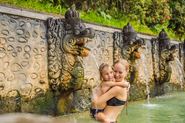 Viajeros de madre e hijo en aguas termales banjar. El agua termal se libera de la boca de estatuas en una fuente termal en Banjar, Bali, Indonesia. Viajar con concepto de niños — Foto de Stock