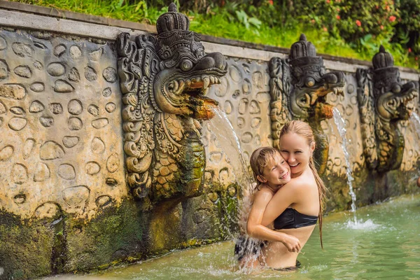 Viajeros de madre e hijo en aguas termales banjar. El agua termal se libera de la boca de estatuas en una fuente termal en Banjar, Bali, Indonesia. Viajar con concepto de niños — Foto de Stock