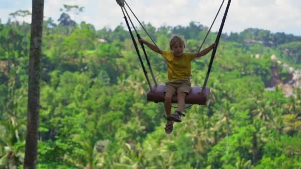 Slowmotion skott av en liten pojke svänger på gungor i en tropisk omgivning. Res till Bali-konceptet — Stockvideo