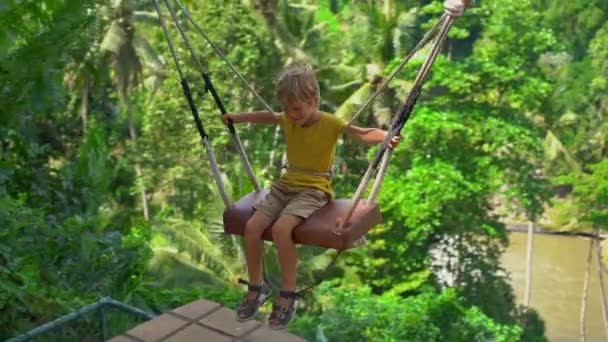 Langzame opname van een kleine jongen die zwaait op schommels in een tropische omgeving. Reis naar Bali concept — Stockvideo