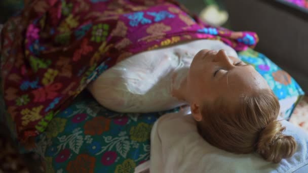 Slowmotion Closeup shot of a young woman in a tropical spa.beautician applies skin moisturizer compound on her skin — Stok Video