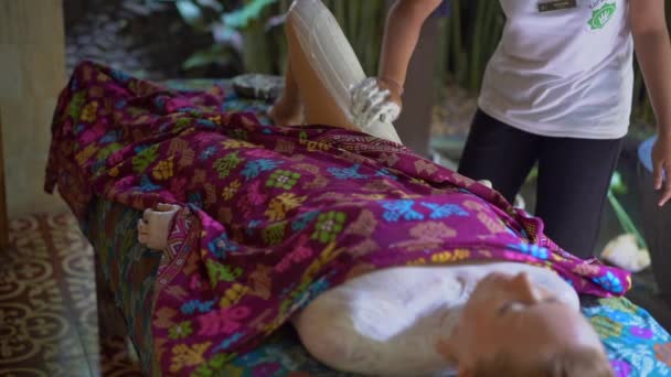 Bali, Indonesia - 5 de junio de 2019. Primer plano en cámara lenta de una mujer joven en un spa.beautician tropical aplica compuesto hidratante de la piel en su piel — Vídeo de stock