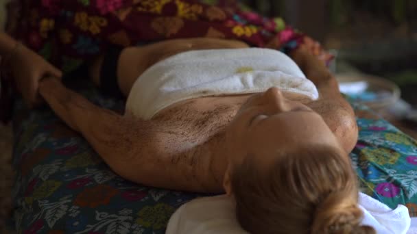 Крупный план молодой женщины в тропическом спа. косметолог применяет скраб кожи тела — стоковое видео