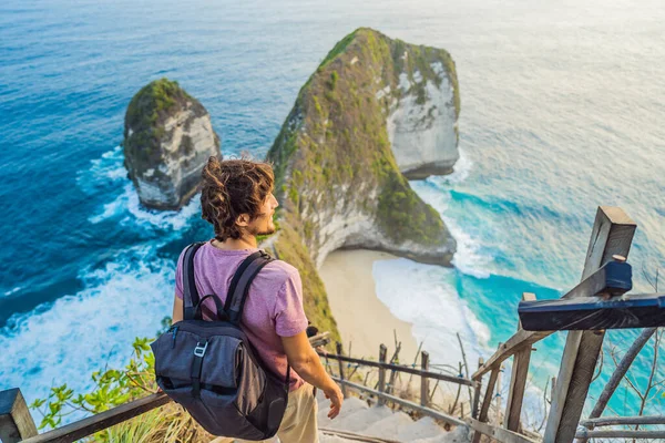 Estilo de vida de vacaciones familiar. Hombre feliz de pie en el punto de vista. Mira la hermosa playa bajo un alto acantilado. Destino de viaje en Bali. Lugar popular para visitar en la isla de Nusa Penida — Foto de Stock