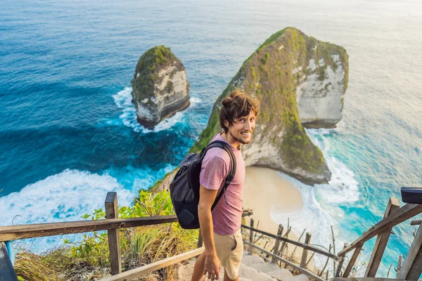 Estilo de vida de vacaciones familiar. Hombre feliz de pie en el punto de vista. Mira la hermosa playa bajo un alto acantilado. Destino de viaje en Bali. Lugar popular para visitar en la isla de Nusa Penida — Foto de Stock