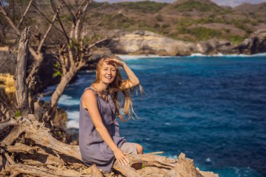 Endonezya 'da, Nusa Penida' da, Melek Billabong 'un arka planında bir ağaçta oturan kadın. Bali Seyahat Konsepti