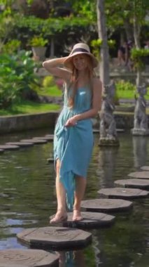 Dikey video. Endonezya 'nın Bali Adası' ndaki eski kraliyet sarayı Tirta Gangga su sarayını ziyaret eden genç bir kadın turist.