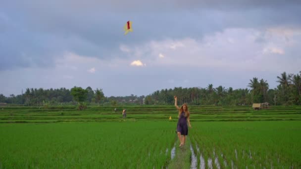 Slowmotion skott av en ung kvinna med en drake går genom en stor vacker risfält — Stockvideo