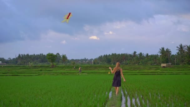 Медленный снимок молодой женщины с воздушным змеем, идущей по большому красивому рисовому полю — стоковое видео