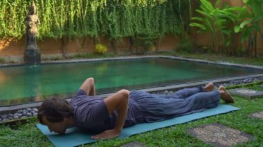 Genç adam yüzme havuzunda yoga yapıyor.