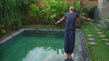 Genç adam yüzme havuzunda yoga yapıyor.