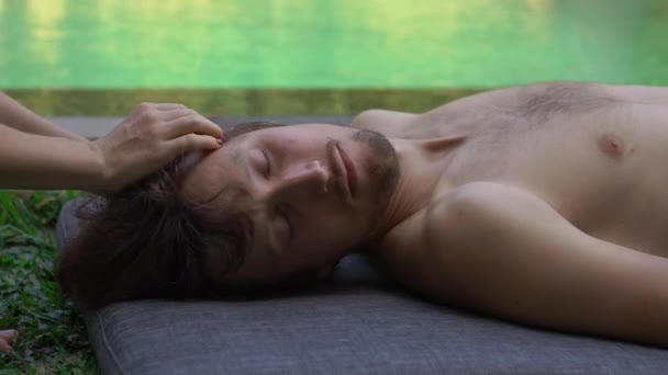 Een close-up van een vrouwelijke therapeut die een massage maakt voor een jonge man bij een zwembad in zijn privé villa. home massage service — Stockvideo