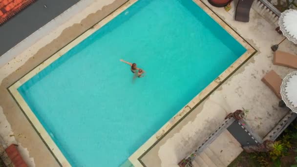 Foto aérea de una joven y su hijo pequeño turistas pasándola bien en una piscina en un entorno tropical. Concepto de vida tropical — Vídeos de Stock