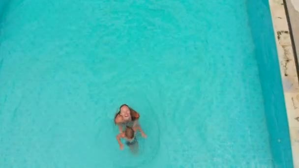 Foto aérea de una joven y su hijo pequeño turistas pasándola bien en una piscina en un entorno tropical. Concepto de vida tropical — Vídeos de Stock