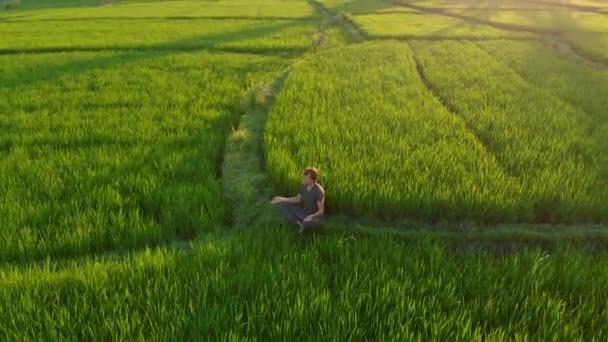 Tiro aéreo de um homem meditando em um maravilhoso campo de arroz durante o pôr-do-sol — Vídeo de Stock