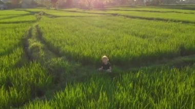 Gün batımında, harika bir pirinç tarlasında meditasyon yapan küçük bir çocuğun hava görüntüsü.