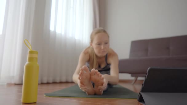 Fitness-Frau trainiert zu Hause auf dem Boden und schaut sich Fitness-Videos auf einem Tablet an. Menschen treiben wegen des Coronovirus online Sport — Stockvideo