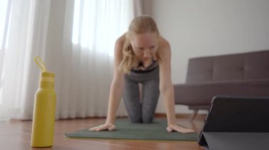 Spor salonundaki kadın evde egzersiz yapıyor ve tabletle spor salonu videoları izliyor. İnsanlar koronovirüs yüzünden spor yapıyor.