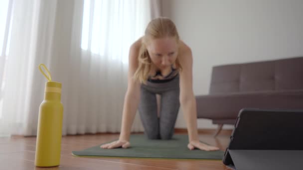 Mujer fitness haciendo ejercicio en el suelo en casa y viendo videos de fitness en una tableta. La gente hace deportes en línea debido al coronovirus — Vídeos de Stock