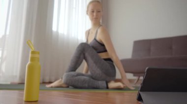 Spor salonundaki kadın evde egzersiz yapıyor ve tabletle spor salonu videoları izliyor. İnsanlar koronovirüs yüzünden spor yapıyor.