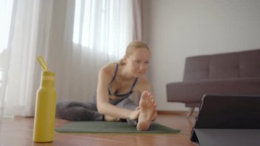 Spor salonundaki kadın evde egzersiz yapıyor ve tabletle spor salonu videoları izliyor. İnsanlar koronovirüs yüzünden spor yapıyor.