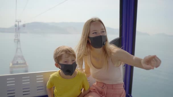 Une jeune femme et son fils portant un masque noir roulent dans un téléphérique ou un téléphérique ou un tramway aérien au-dessus de la mer. Le verrouillage est terminé, mais les gens doivent porter des masques partout. Réouverture économique — Video