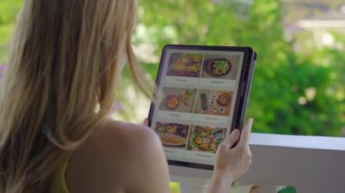 Genç bir kadın, tablet kullanarak internetten yemek sipariş ediyor. Dairesinde bir balkonda oturuyor.