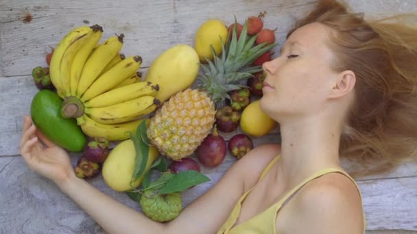 Parte superior de la vista: una mujer sostiene un corazón hecho de muchas frutas tropicales. Concepto vegetariano — Vídeos de Stock